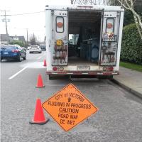 City sign notifying of flushing in progress with truck in background.